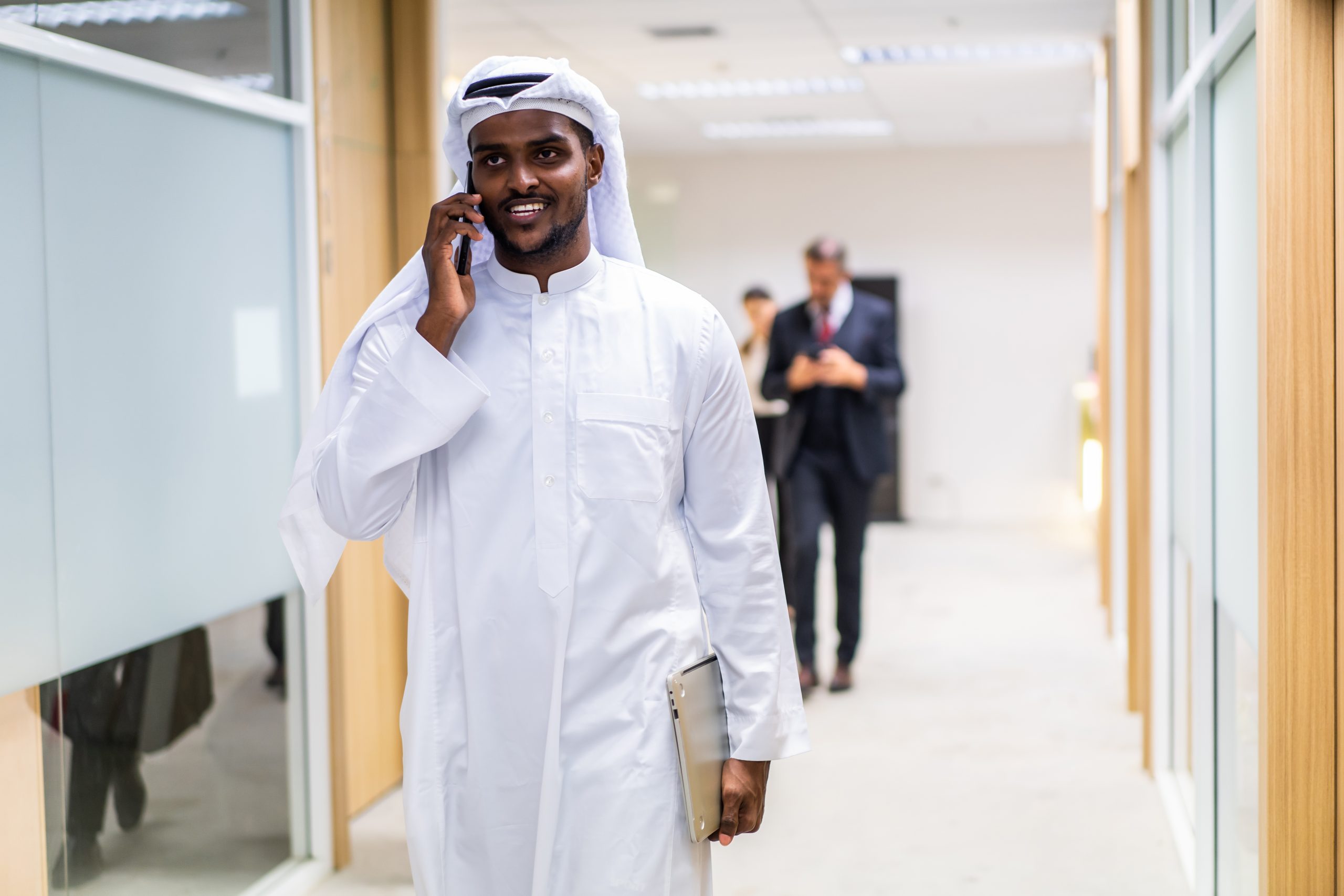 arab-businessman-using-smartphone-while-standing-i-2025-03-31-03-43-54-utc Arab Businessman using smartphone while standing in corridor of office. Attractive male employee chatting and communicate on mobile phone with colleagues indoors with confidence in corporate workplace