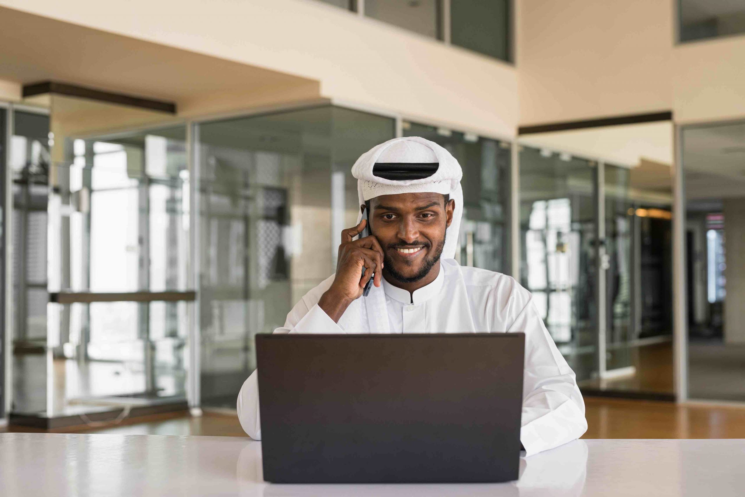 Young African Muslim man using laptop computer and phone at office